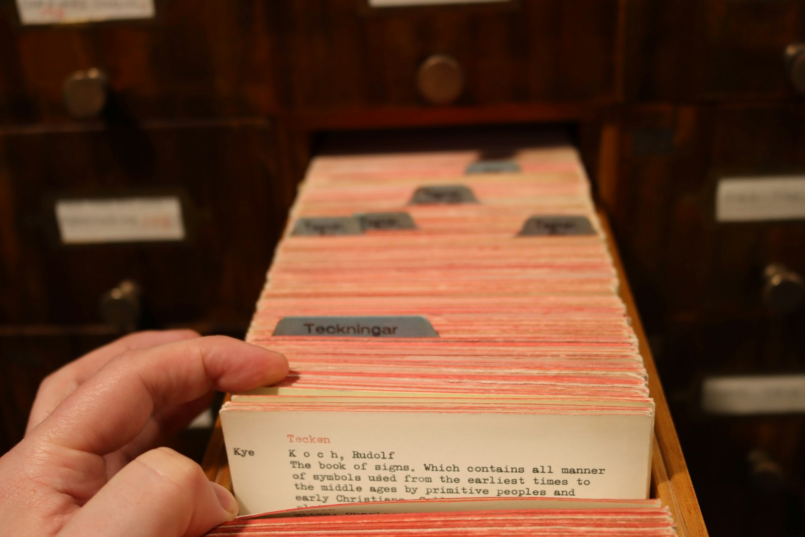 A hand pulls a card from the library's card catalog