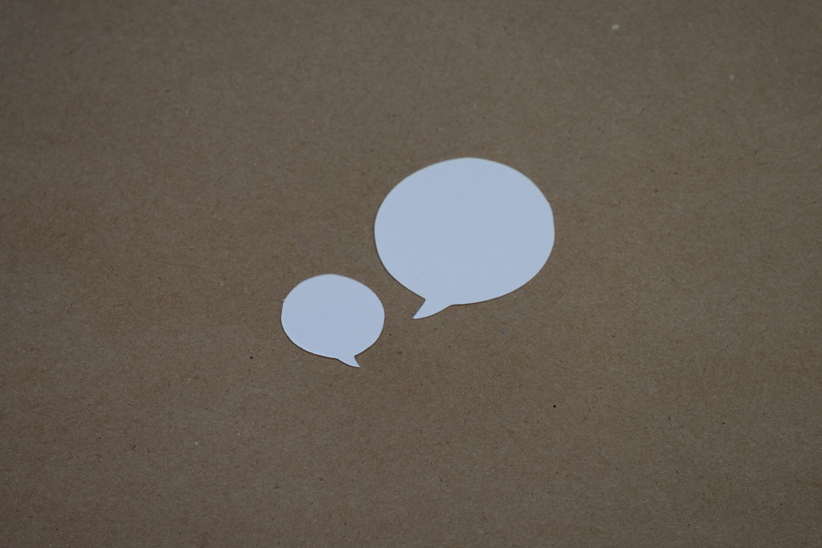 Two white speech bubbles sitting on top of a brown surface